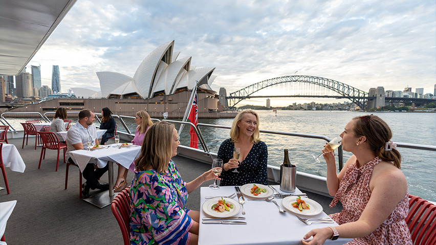 People dining on a lunch cruise in Sydney, with the Opera House and Harbour Bridge in the background